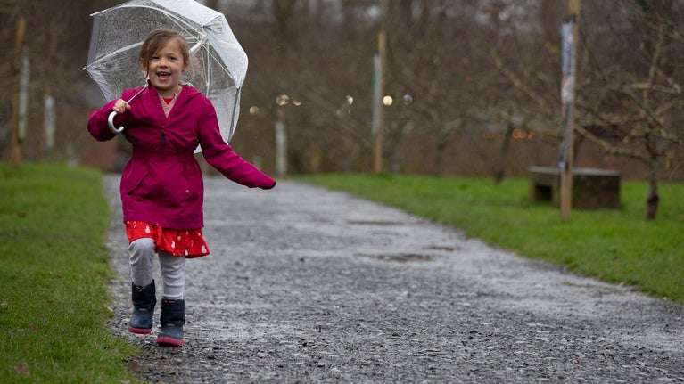 A child with a clear umbrella smiling in the rain.